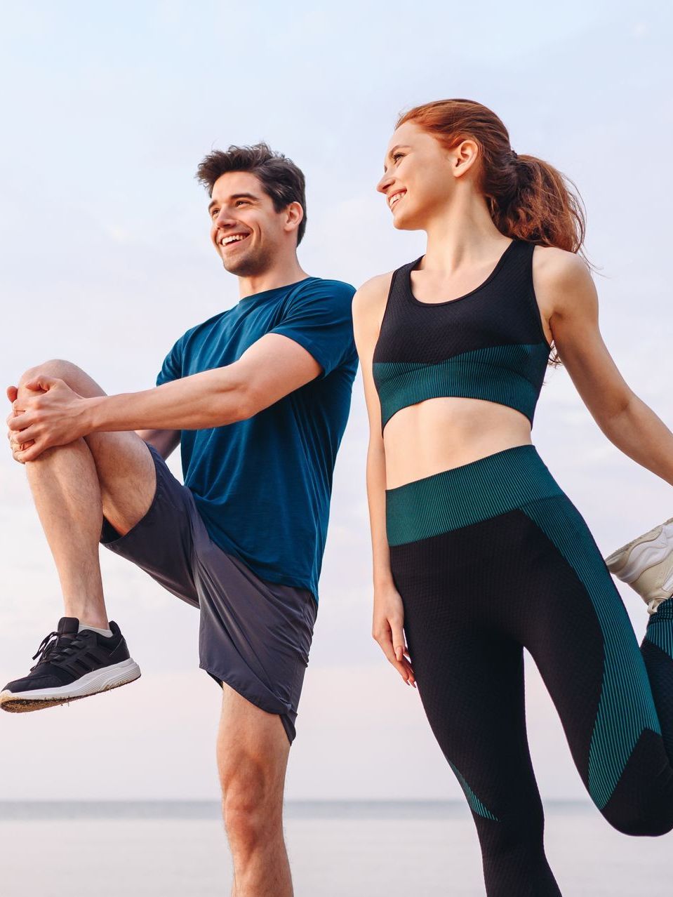 A man and a woman are stretching their legs on the beach.