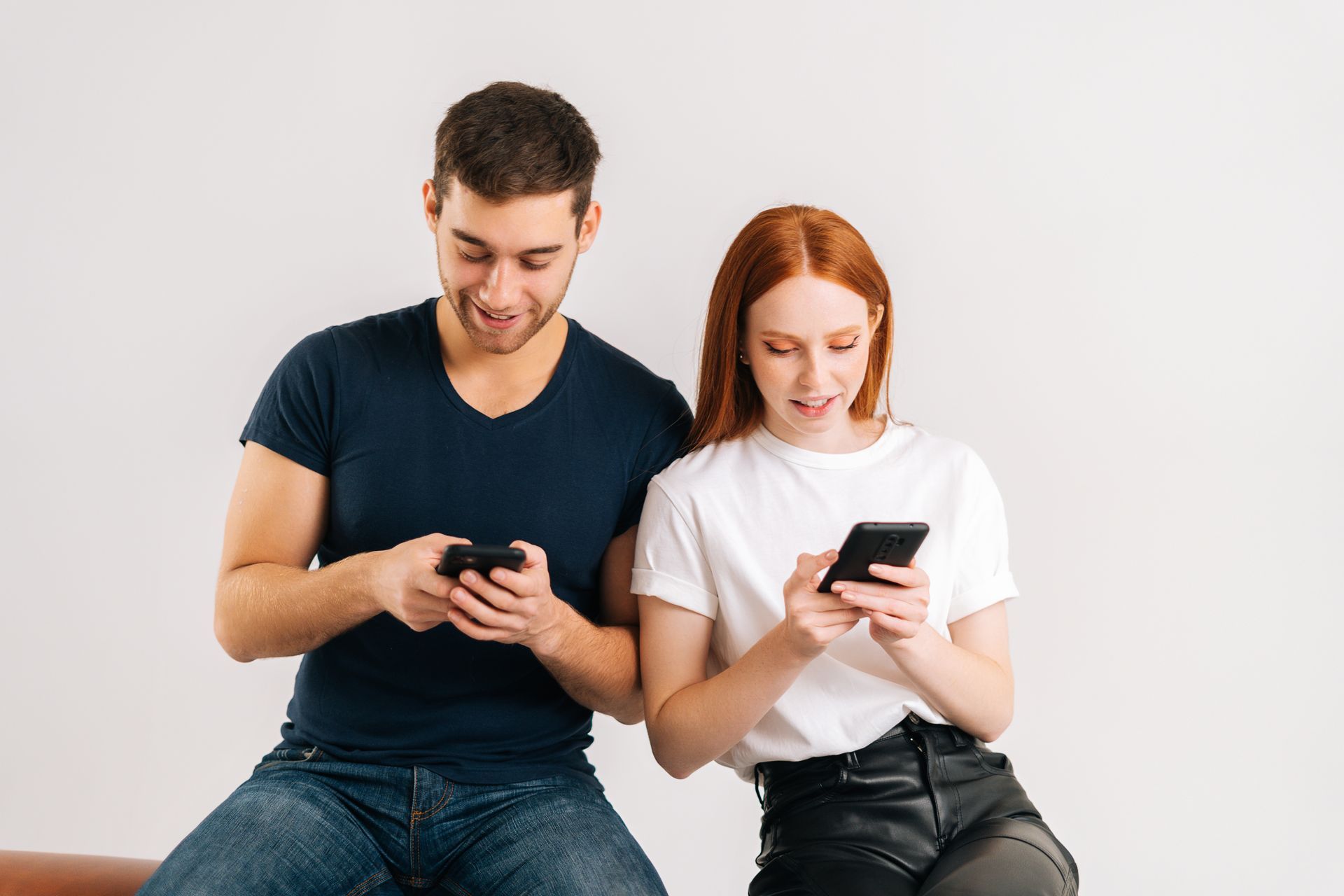 A man and a woman are sitting on a couch looking at their phones.