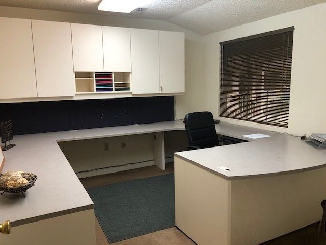 U-shaped office desk with built-in overhead cabinets and a window with blinds.