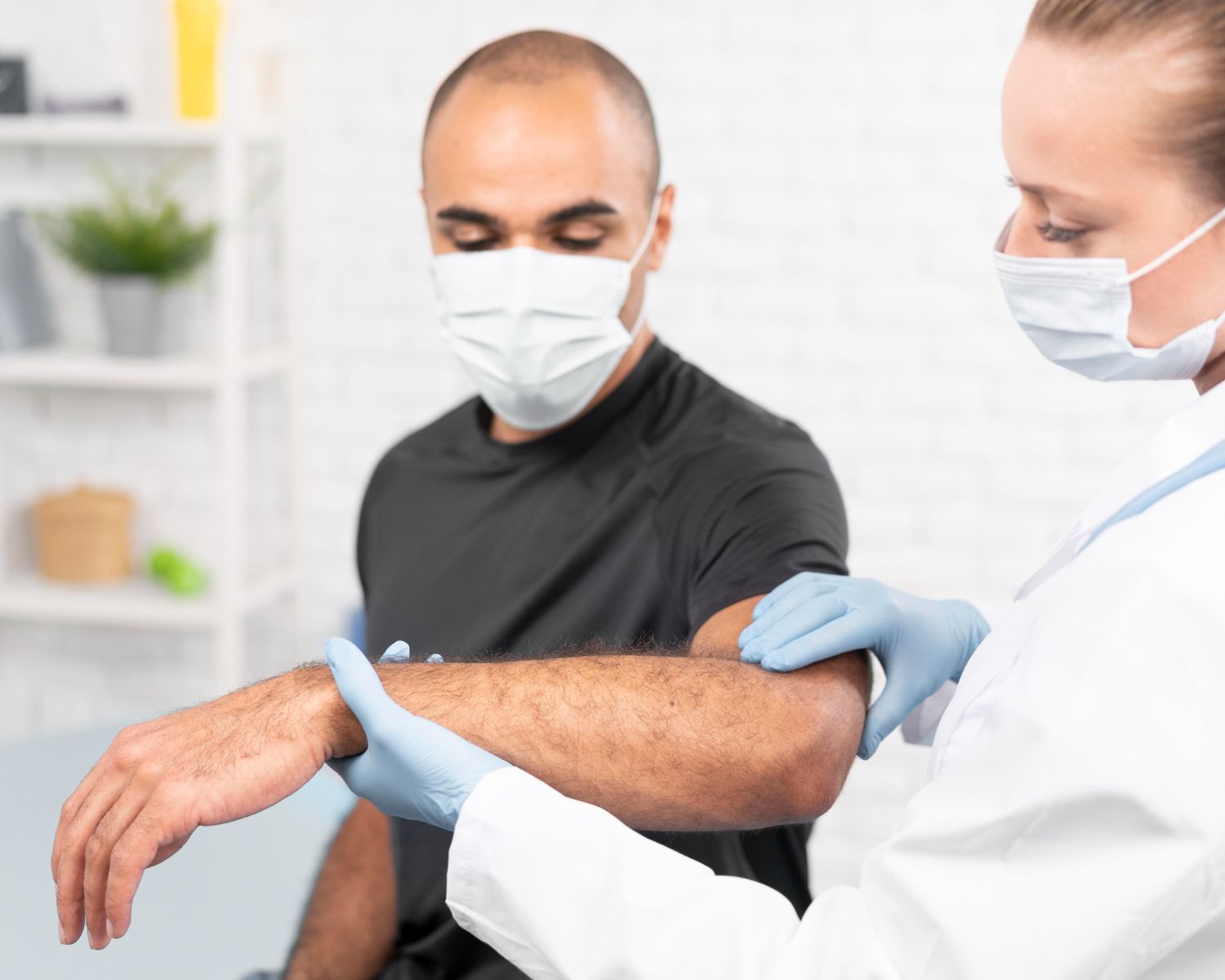 Masked clinician examining a patient’s arm in a bright medical office