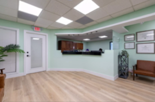 Empty medical office waiting room with pale green walls, wood flooring, and reception desk