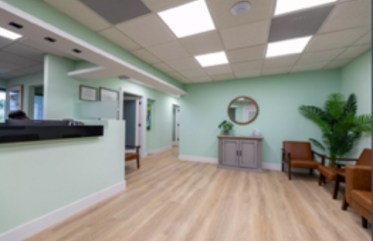 Bright waiting room with mint walls, wood floors, reception desk, chairs, plant, and round mirror.