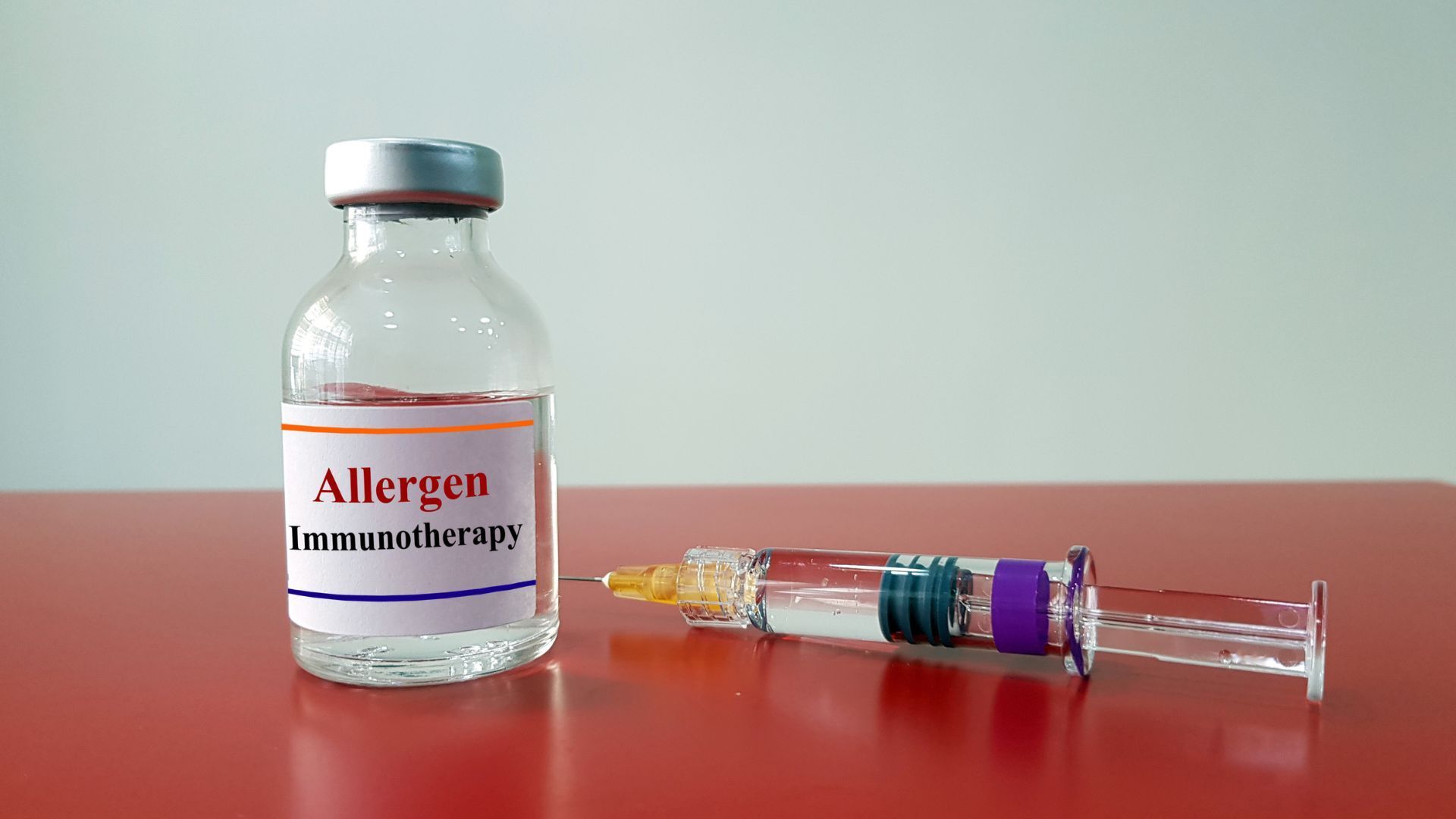 Allergen immunotherapy vial and syringe on a red table against a light blue background