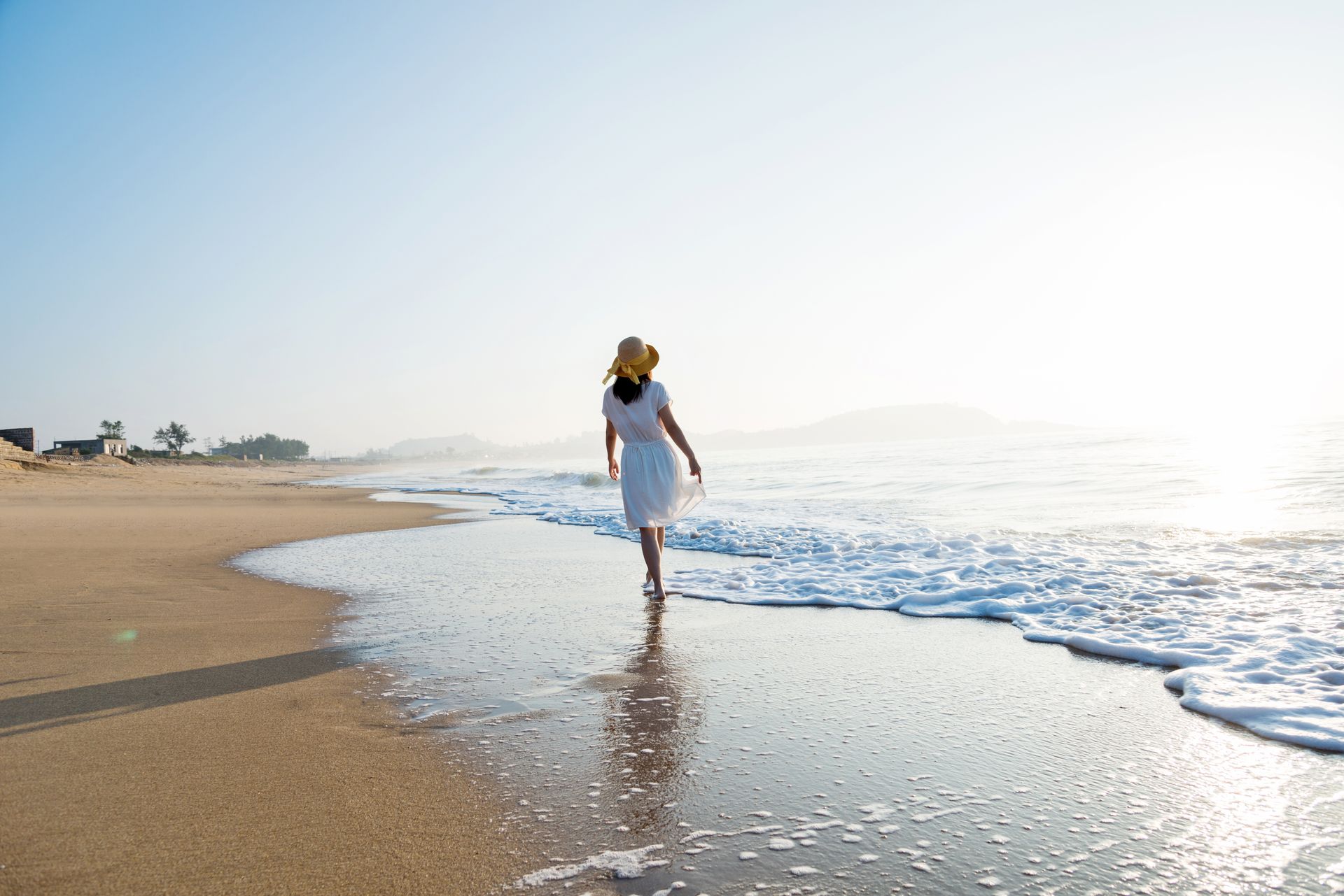 Person walking barefoot along a sandy beach by the shoreline at sunrise