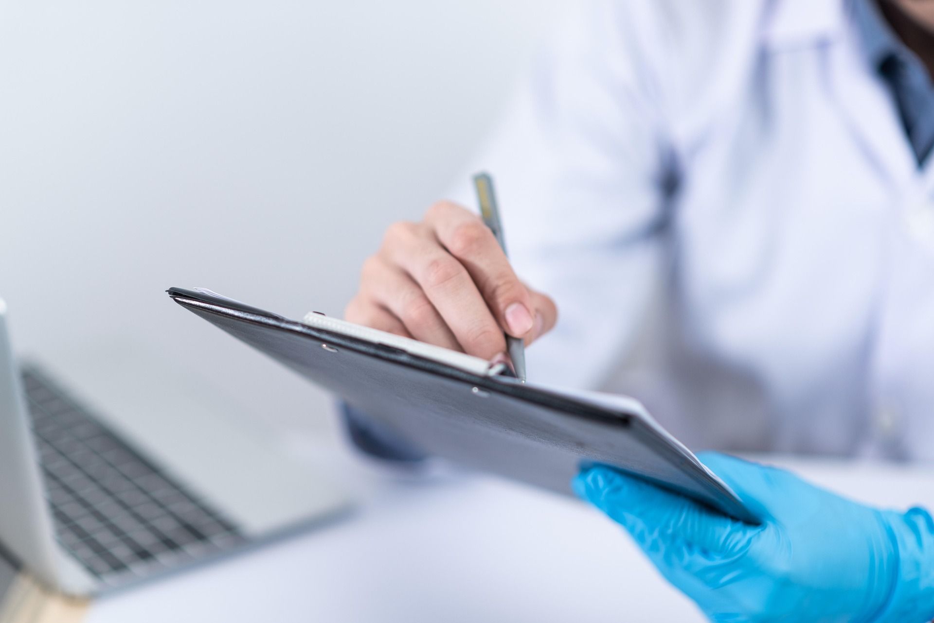 Gloved hand holding a tablet while a doctor uses a stylus in a clinical setting