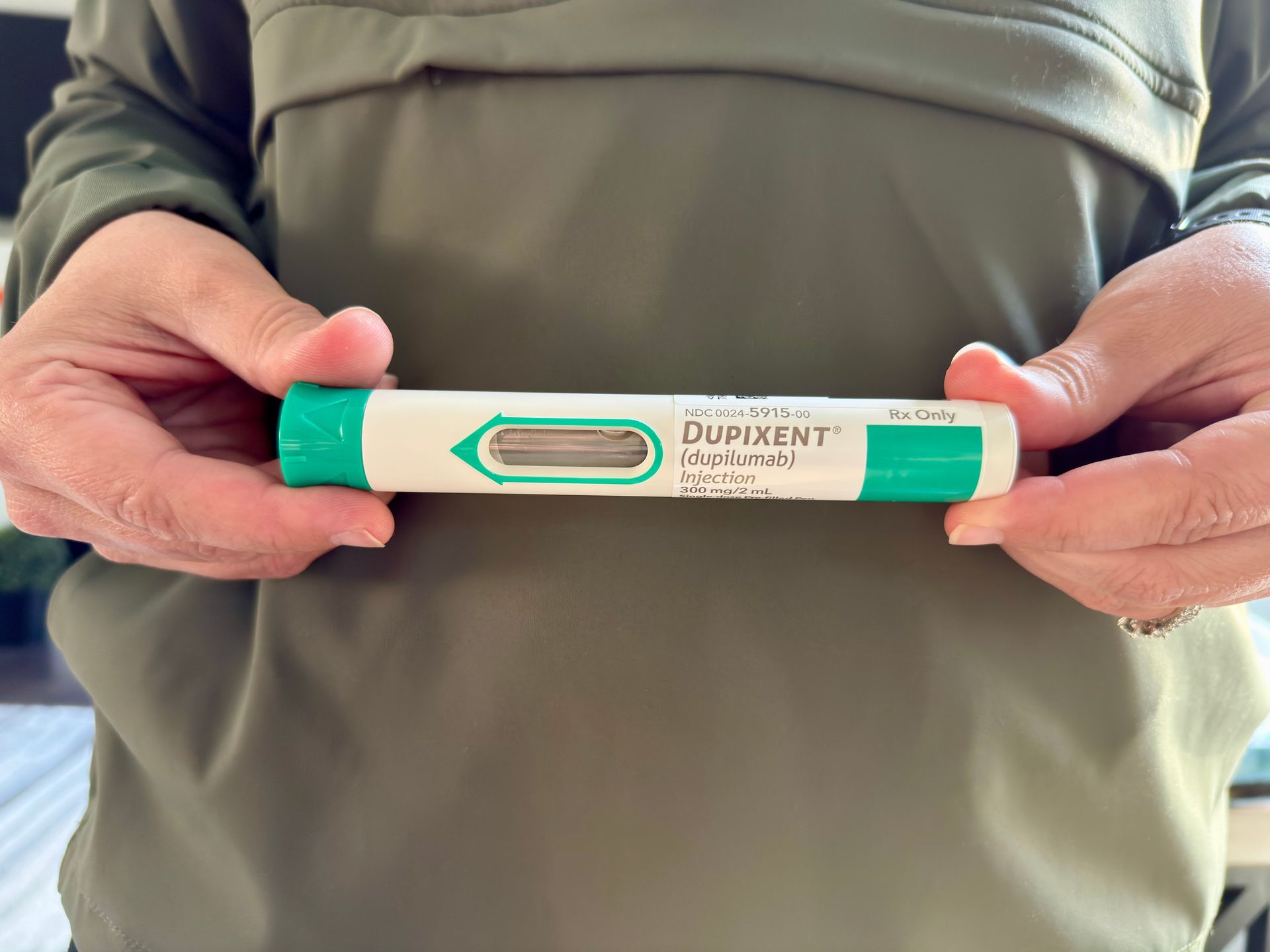 Hands holding a green-and-white DuPEN pen injector against a beige shirt.