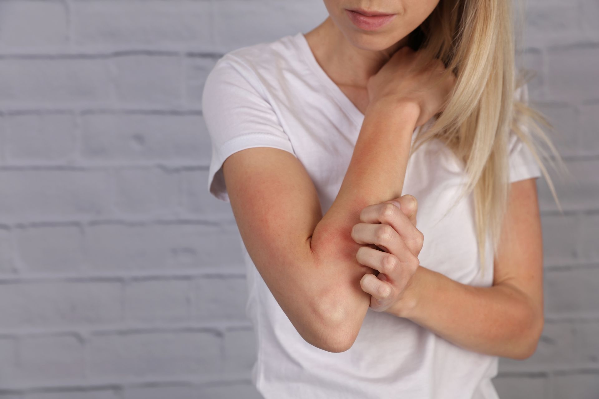 Person in a white shirt holding their elbow against a gray brick wall.