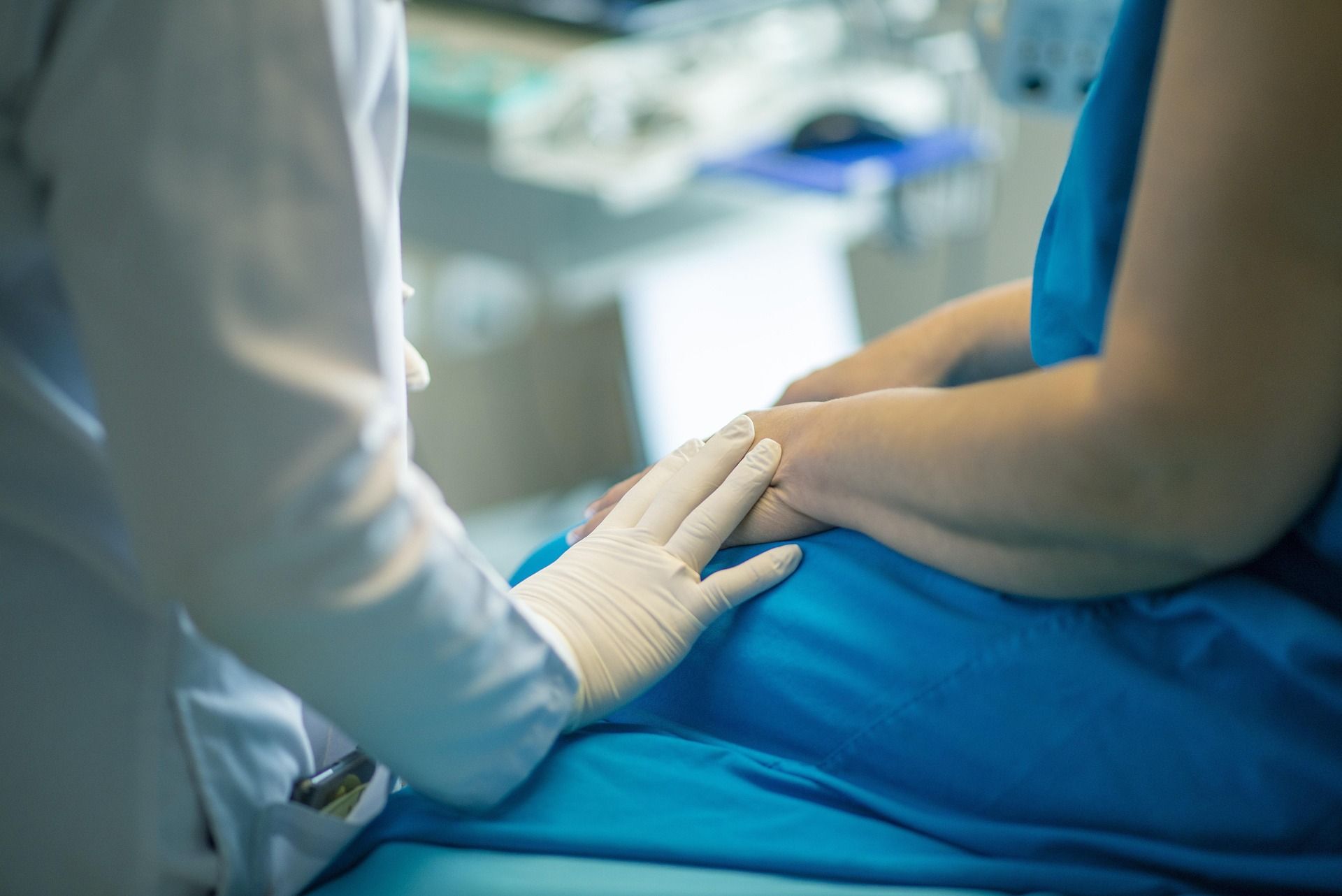 Healthcare worker checking a patient’s arm while seated on a blue hospital bed