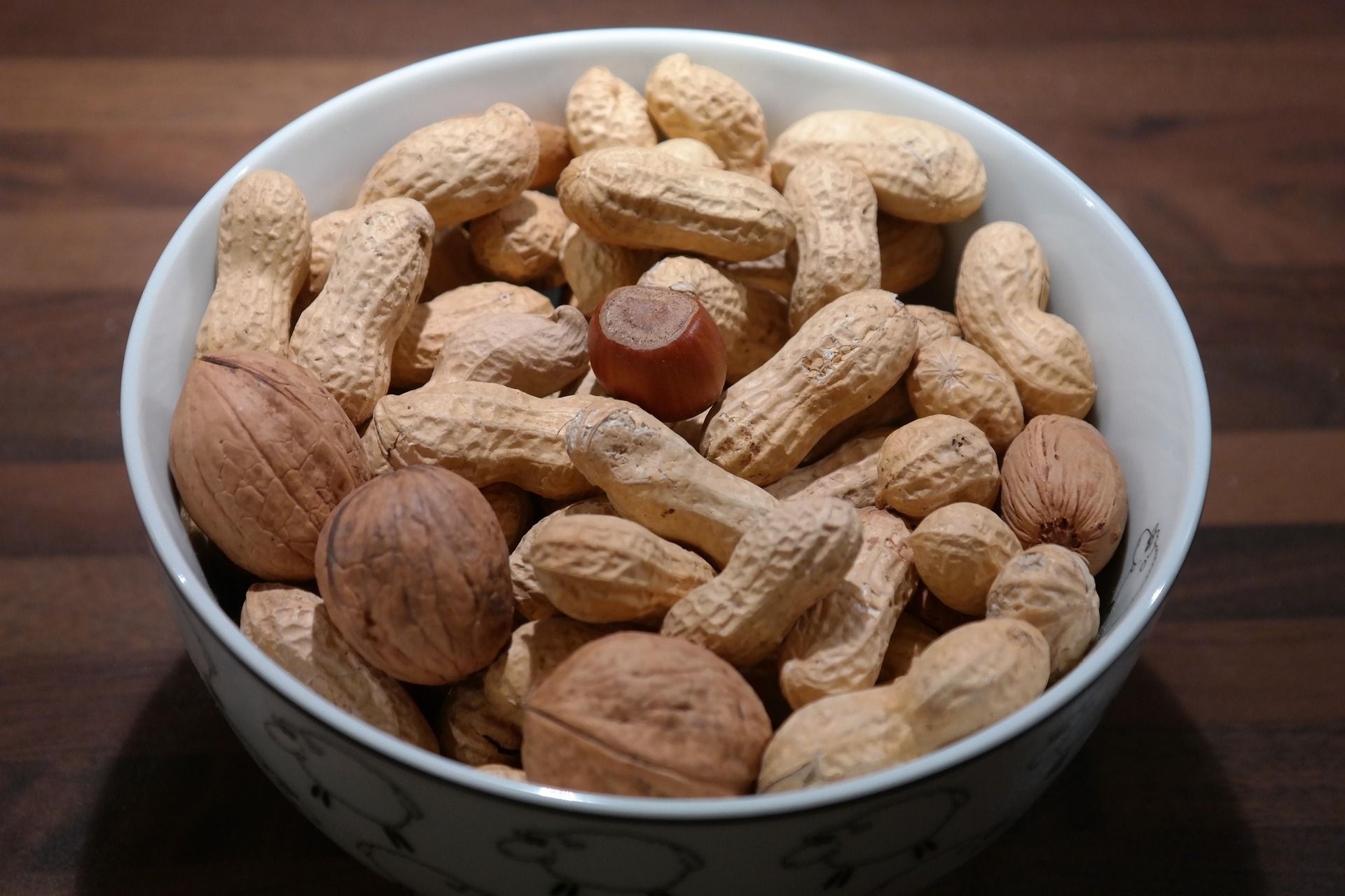 Bowl of unshelled peanuts on a dark surface