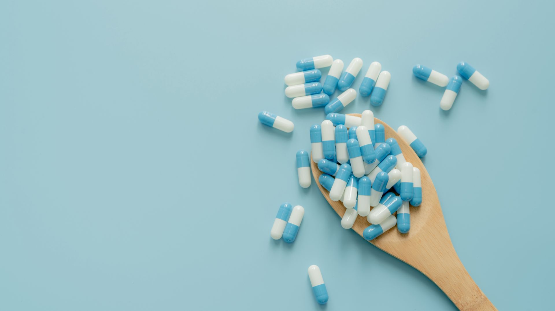 Hand holding scattered blue-and-white capsules on a light blue background