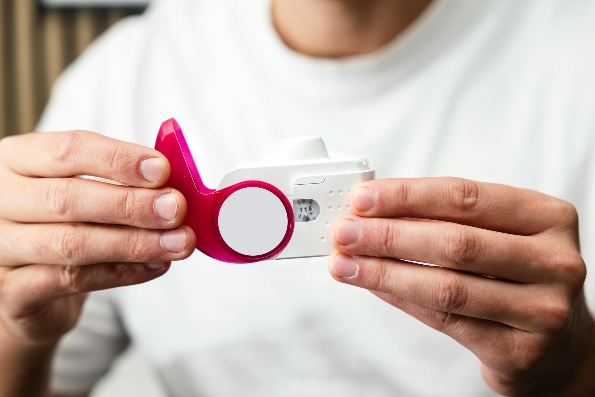Hands holding a white camera with a bright pink strap against a white shirt background