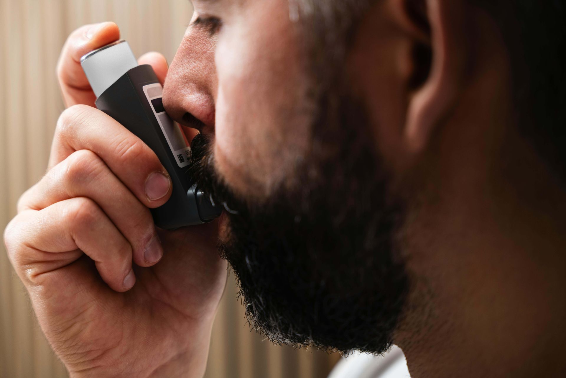 Man using a black inhaler at his mouth, close-up side view