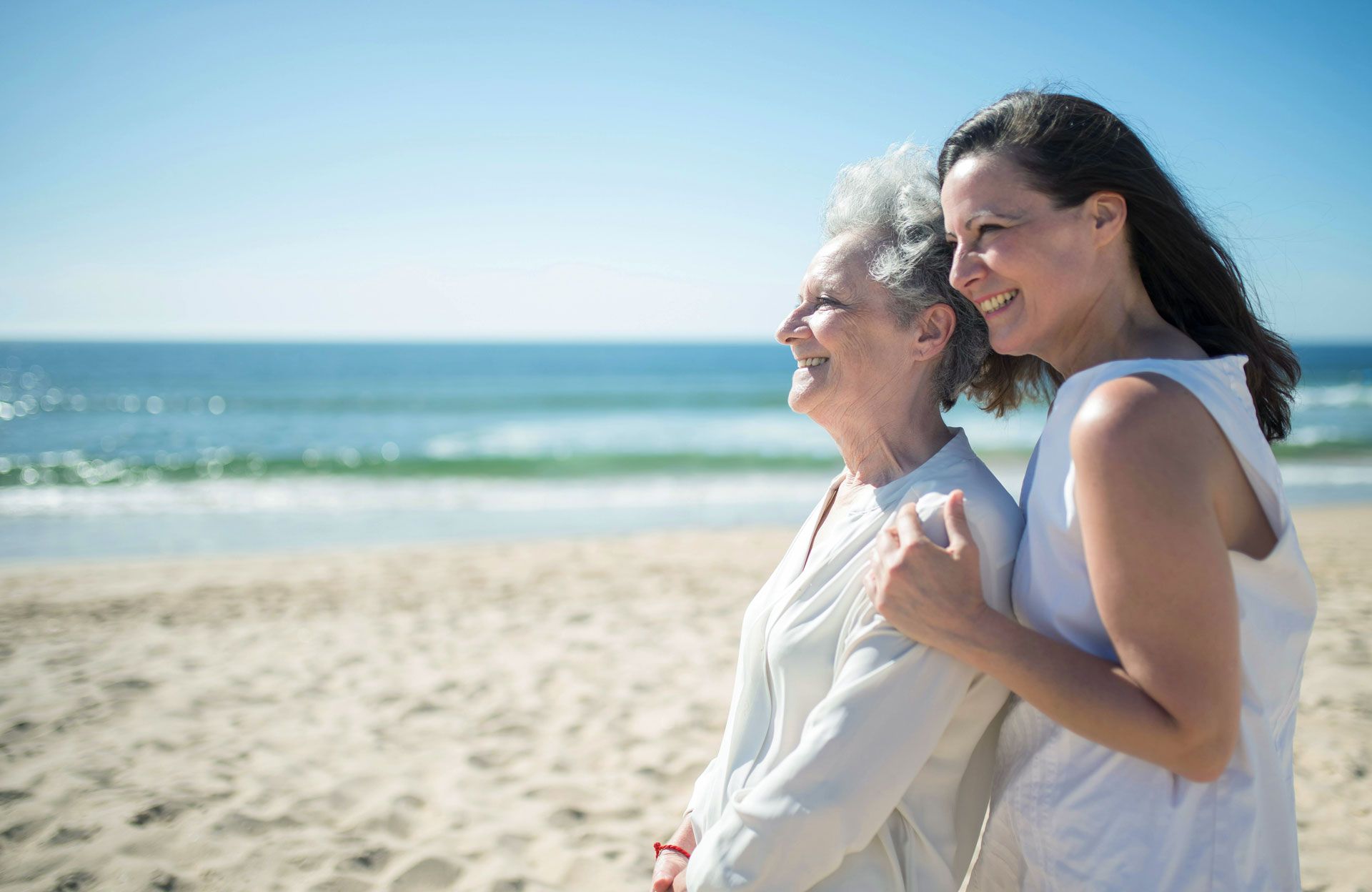 Two people smiling and embracing on a sunny beach with ocean waves in the background