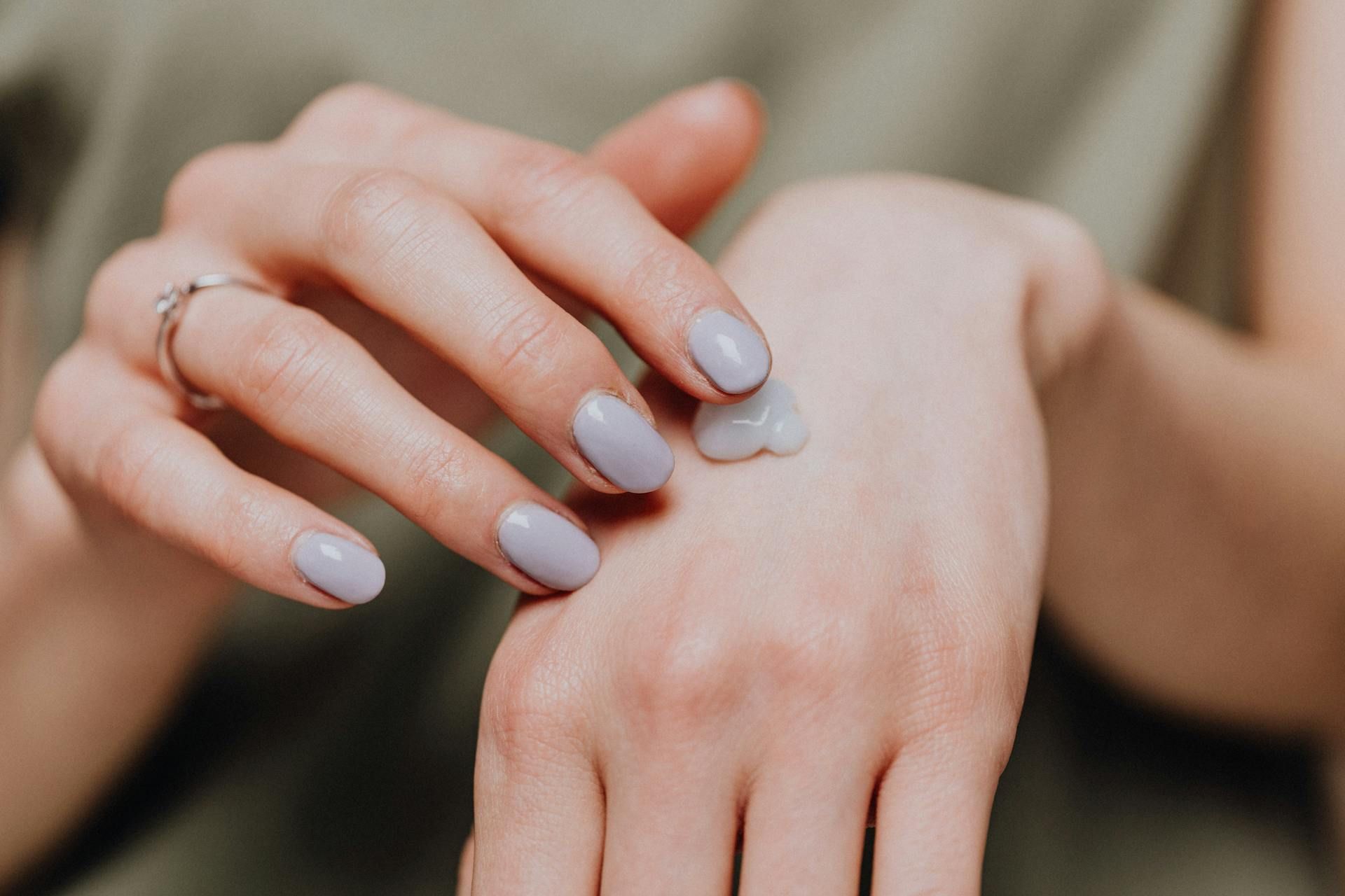 Hands with pale lavender manicured nails gently resting together in soft light