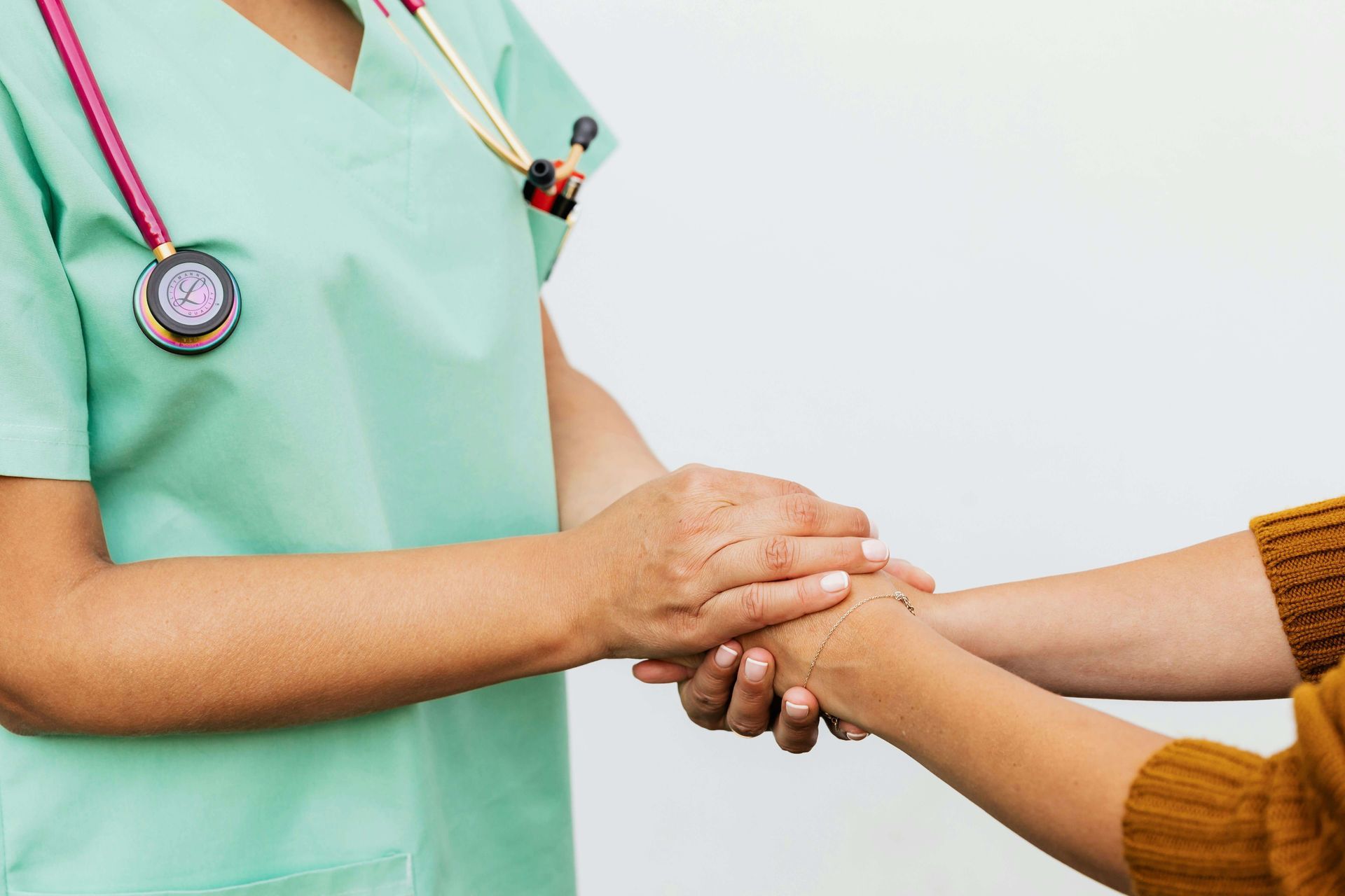 Nurse in green scrubs holding a patient's hand in a clinical setting