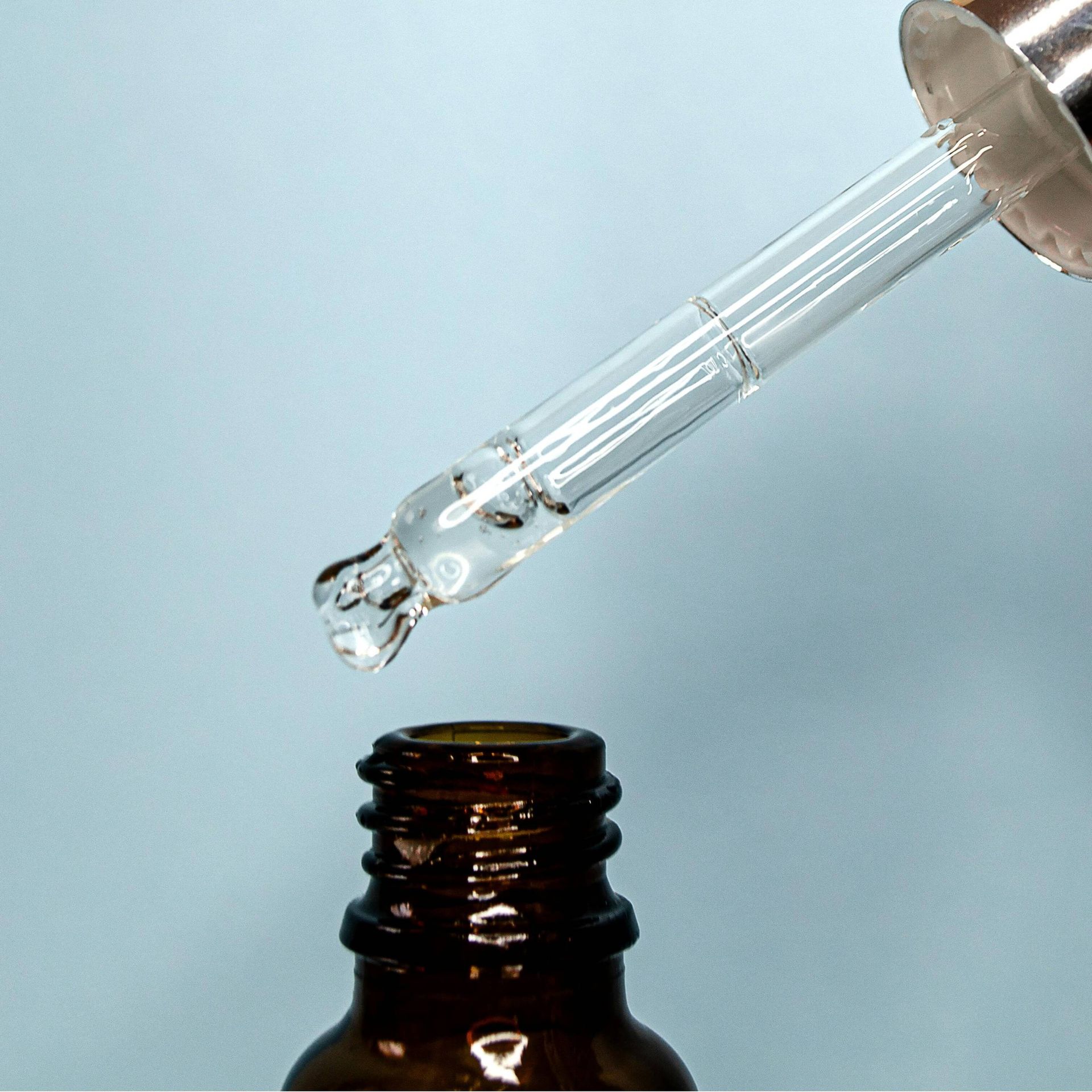 Dropper dispensing clear liquid into an amber glass bottle.
