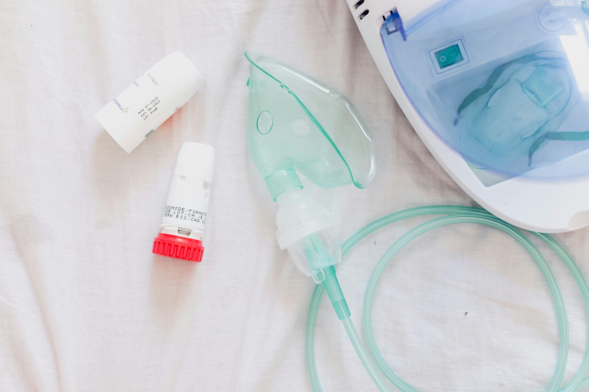 Asthma inhaler, nebulizer mask, and medicine vial on a white surface