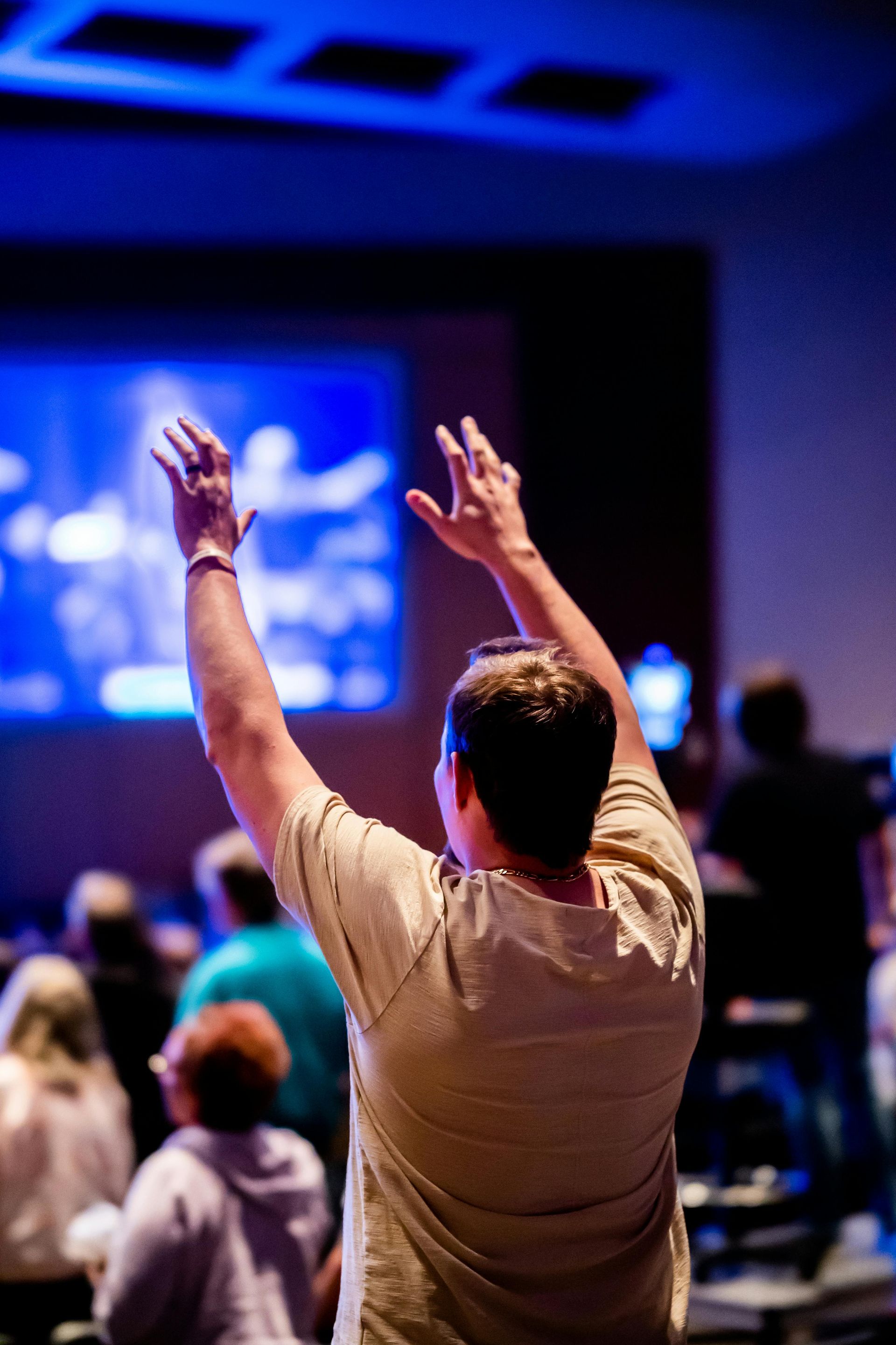 Person raising both hands in a dim conference room facing a blue-lit presentation screen