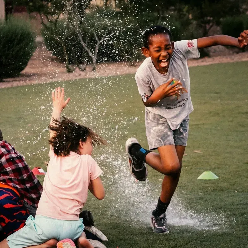 Children laughing and splashing water on a grassy lawn outdoors