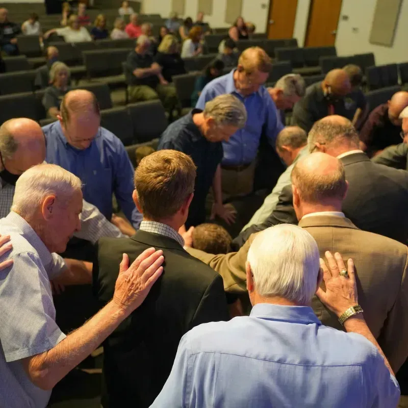 People gathered in a lecture hall, several standing and speaking in a small group.