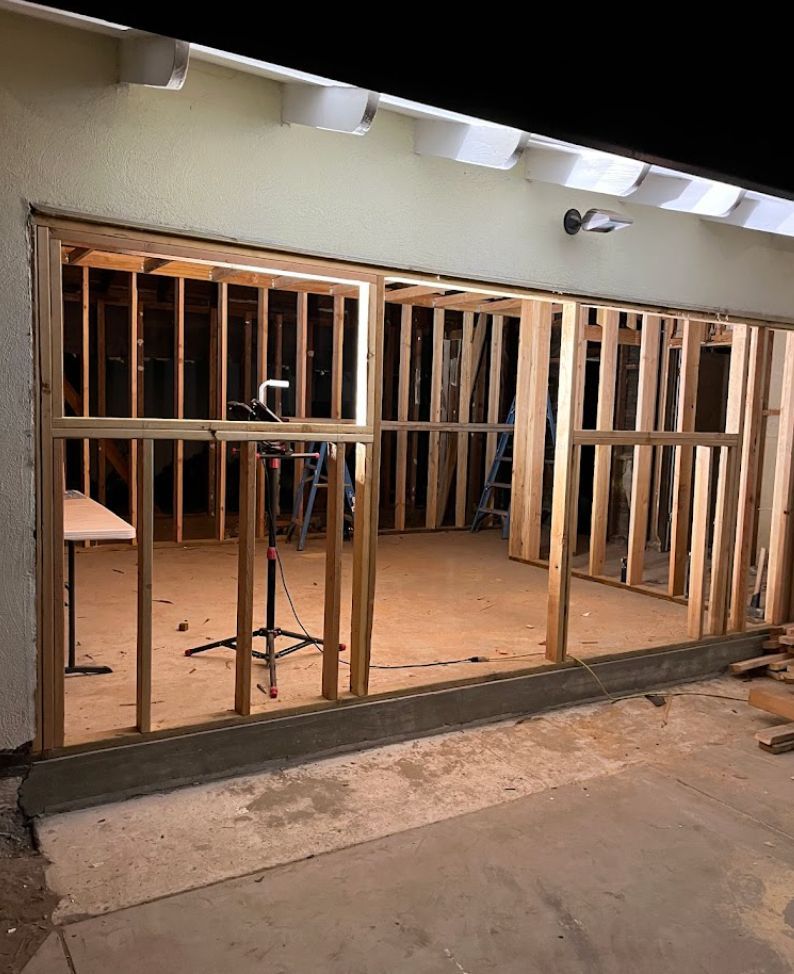 Partially framed wall inside a construction area with exposed wooden studs and concrete floor