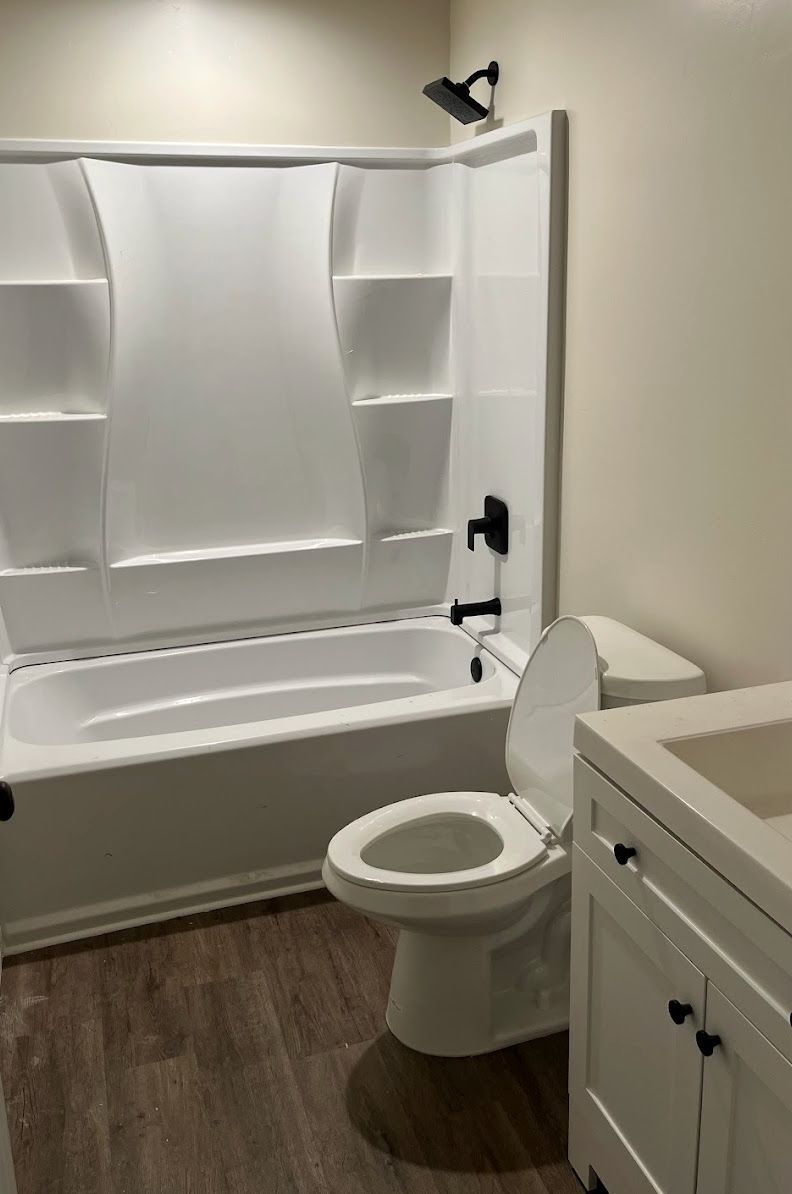 Small bathroom with white tub, shower curtain, toilet, and vanity on wood-look floor