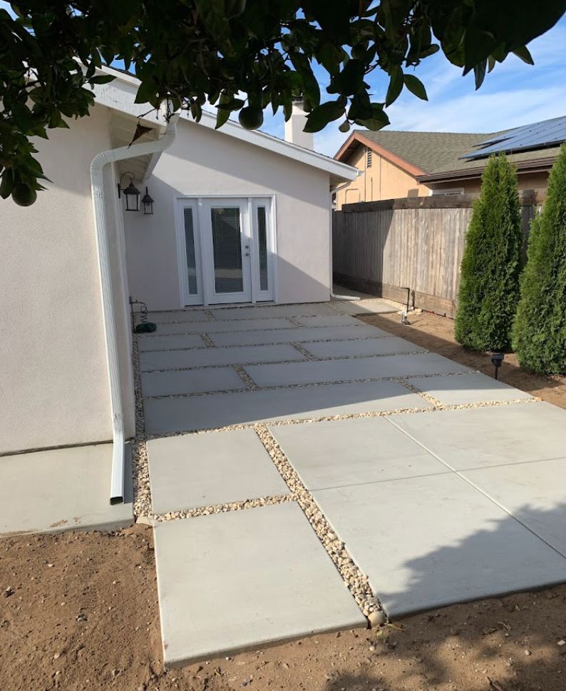 Backyard patio with large concrete pavers, white house exterior, and small gravel accents leading to double doors