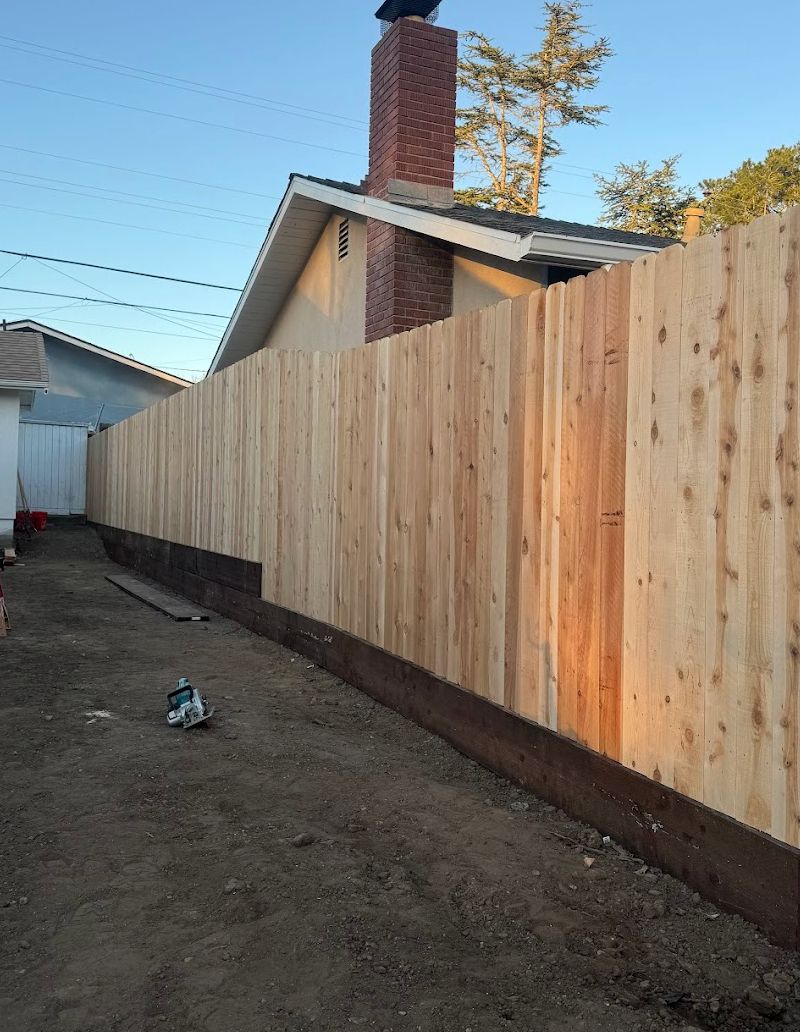 Wooden fence along a dirt alley beside a house with a brick chimney at dusk