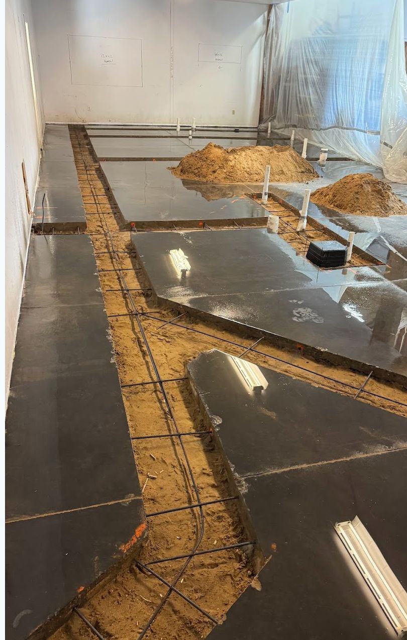 Indoor construction area with a narrow trench lined in orange mesh beside wet concrete floor panels