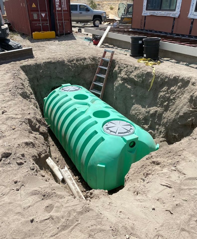 Green septic tank installed in an excavated hole beside a house, with a ladder leaning over it.