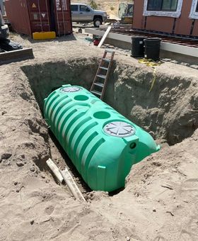 Green septic tank installed in an excavated hole beside a house, with a ladder leaning over it.