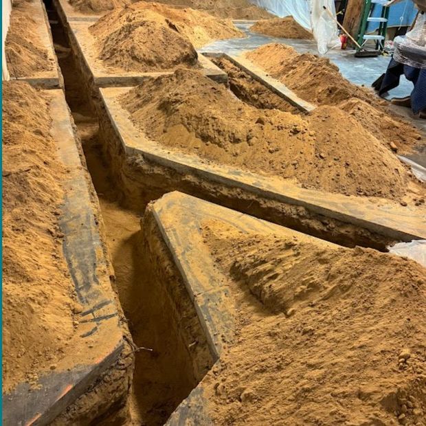 Rows of sand-filled graves at a cemetery, with a few workers visible in the background.