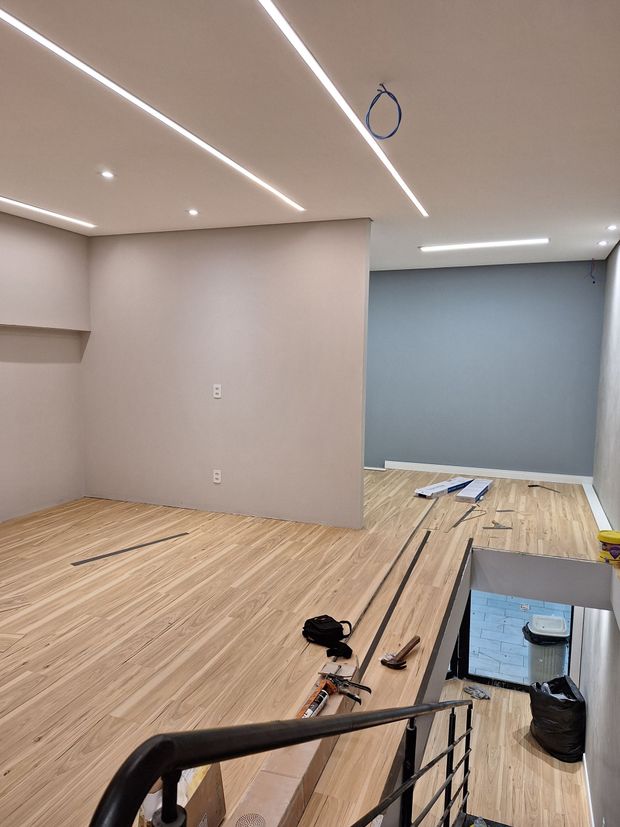 Empty room under renovation with wood flooring, gray walls, ceiling lights, and construction materials on the floor