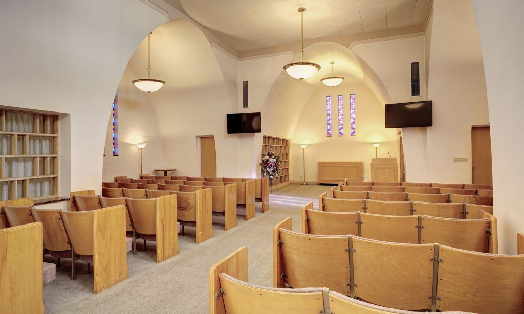 A church with rows of wooden benches and a stained glass window.