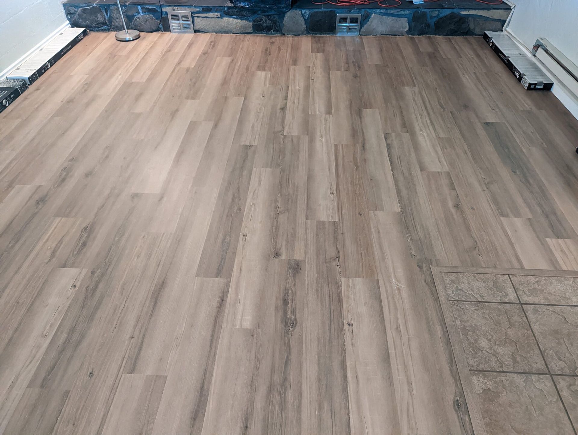 Wood-look vinyl flooring installed in a room, with exposed baseboard trim and unfinished edges.