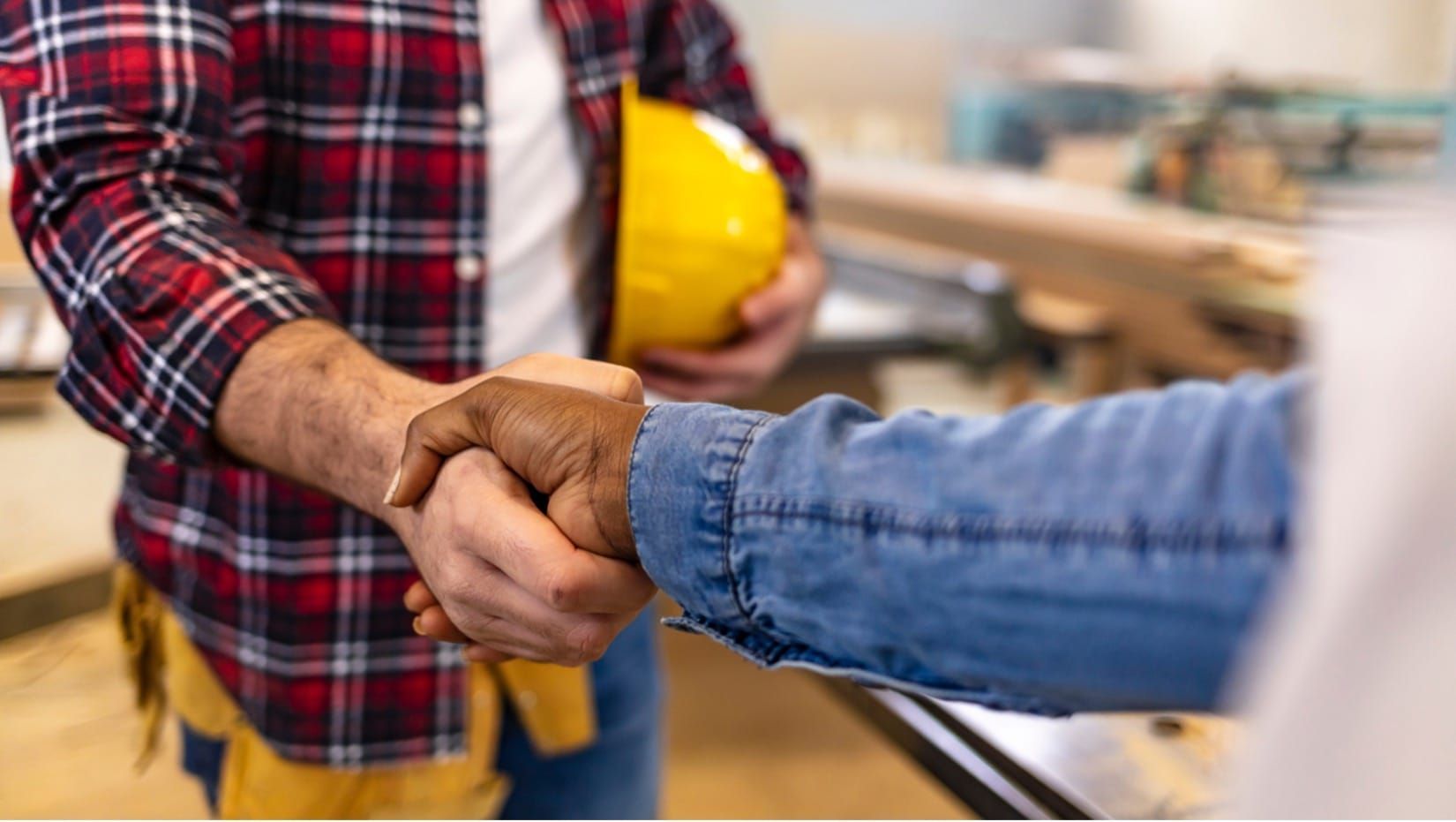 Handing a handshake in a construction setting, with a yellow hard hat in the background