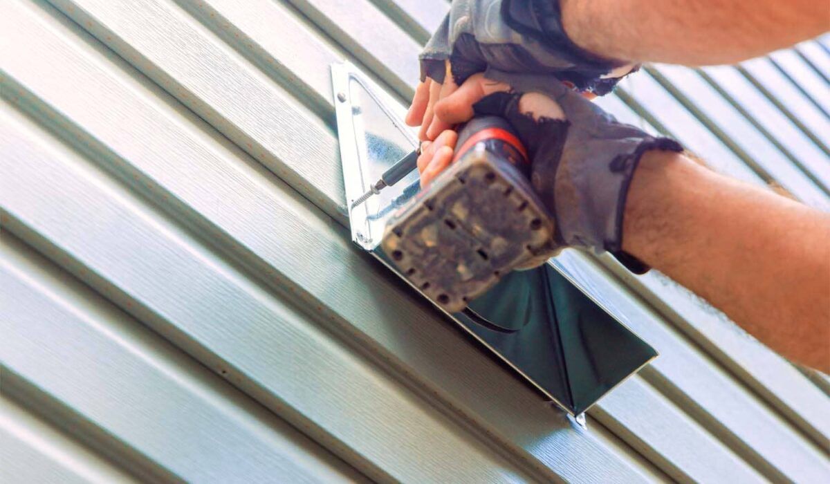 Hands using a power drill to fasten a metal roof panel
