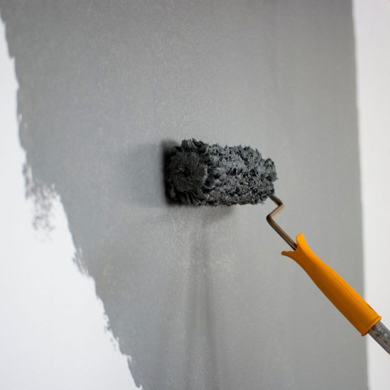 Paint roller applying gray paint to a wall