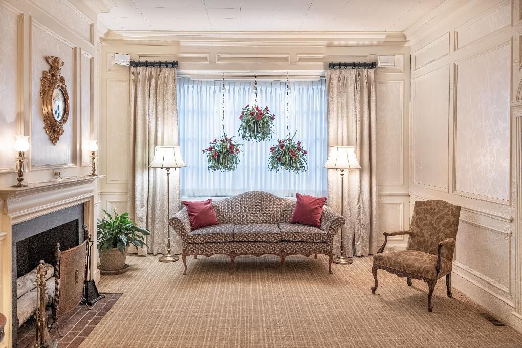 Elegant cream-colored living room with fireplace, sofa, armchair, and floral window arrangement