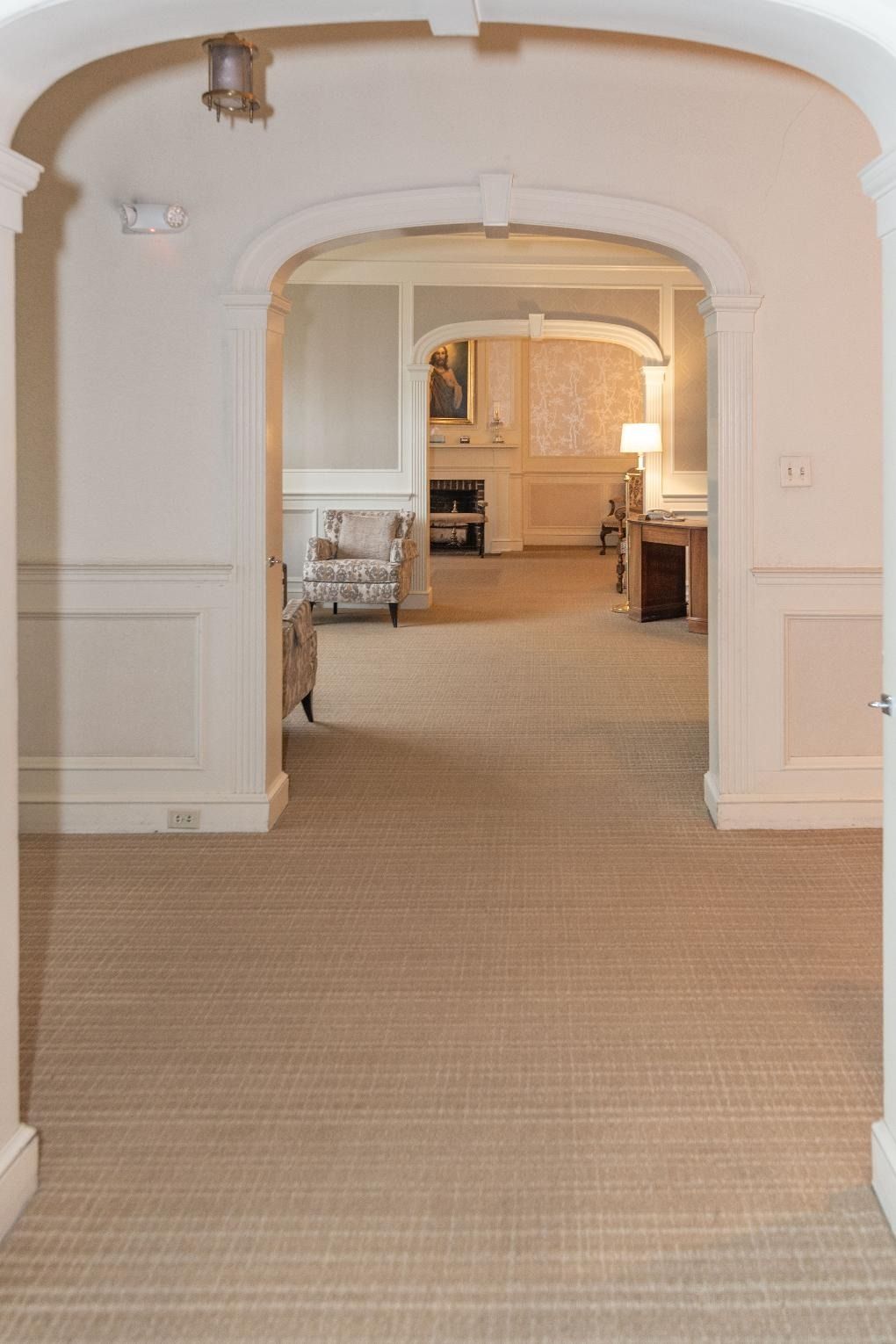 Wide carpeted hallway with white arched doorway opening into a warmly lit room