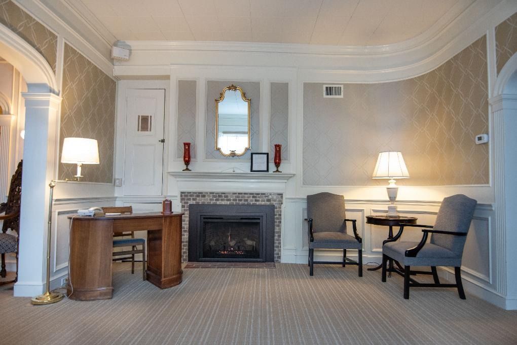 Elegant hotel room with fireplace, desk, mirror, and two armchairs in neutral tones