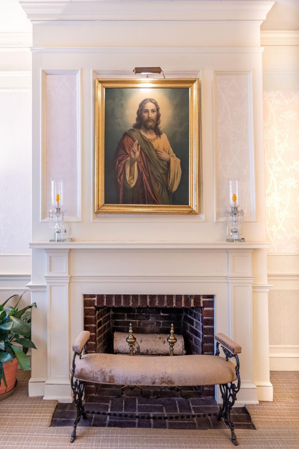 Elegant white fireplace with a framed portrait above and a cushioned bench in front