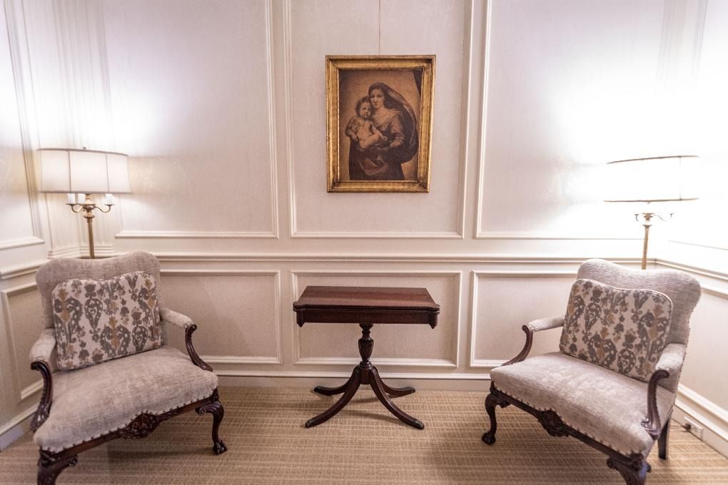 Elegant sitting room with two patterned armchairs, a small table, and a framed painting on a white paneled wall