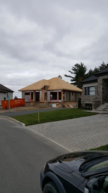 A car is parked in front of a house under construction.