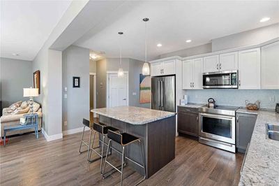 A modern open-plan kitchen with white upper cabinets, dark base cabinets, granite countertops, and a central island.