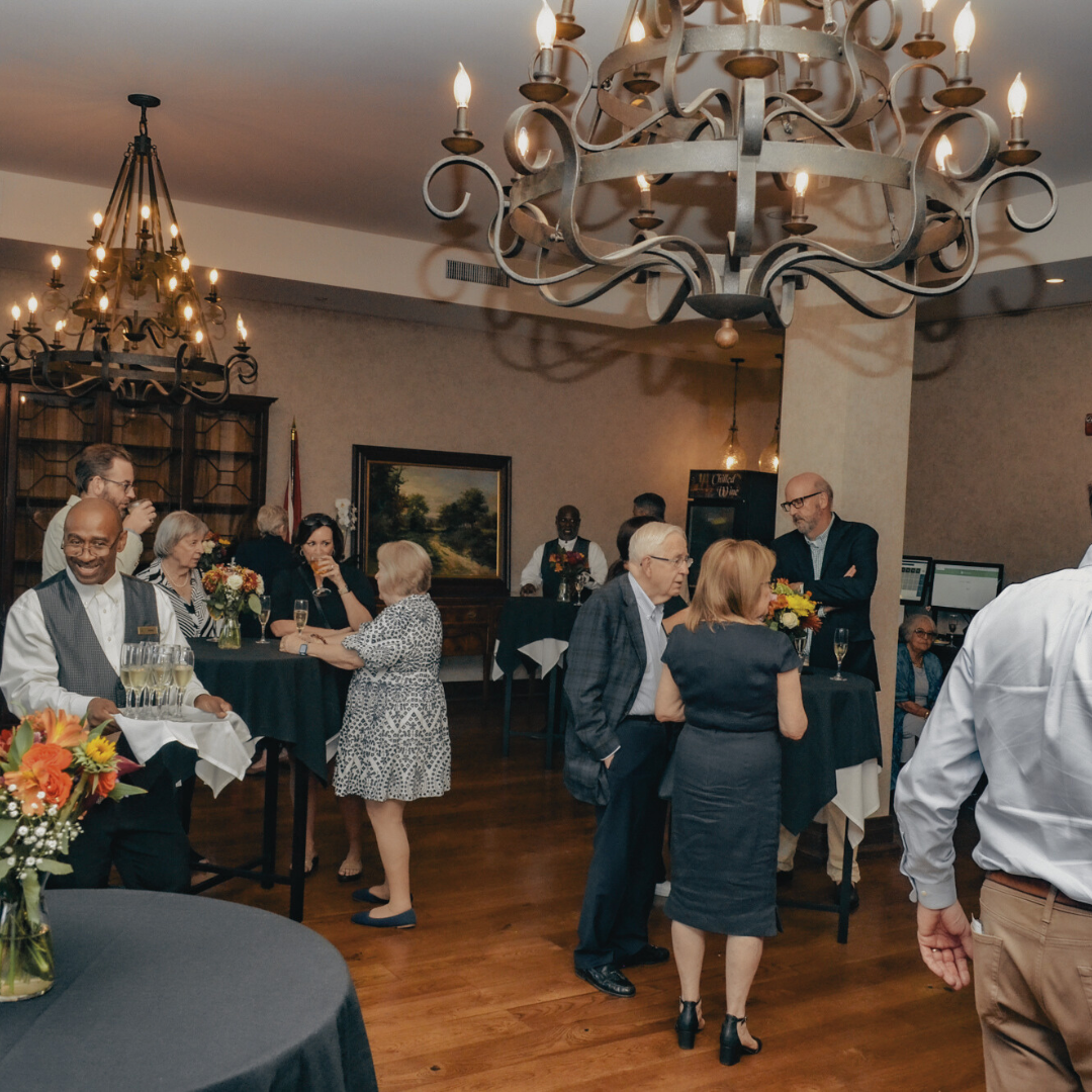 A group of people are gathered in a room with tables and a chandelier