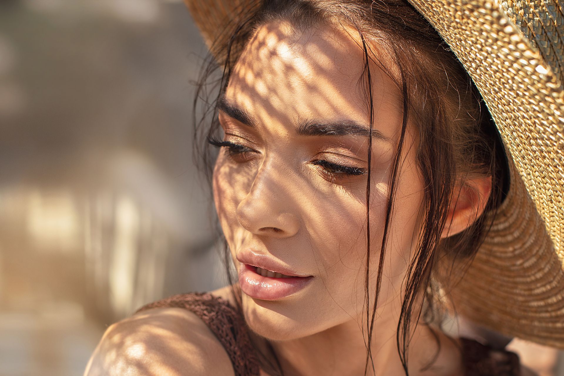 Woman with sun-dappled face wearing a straw hat; looking down with a contemplative expression.