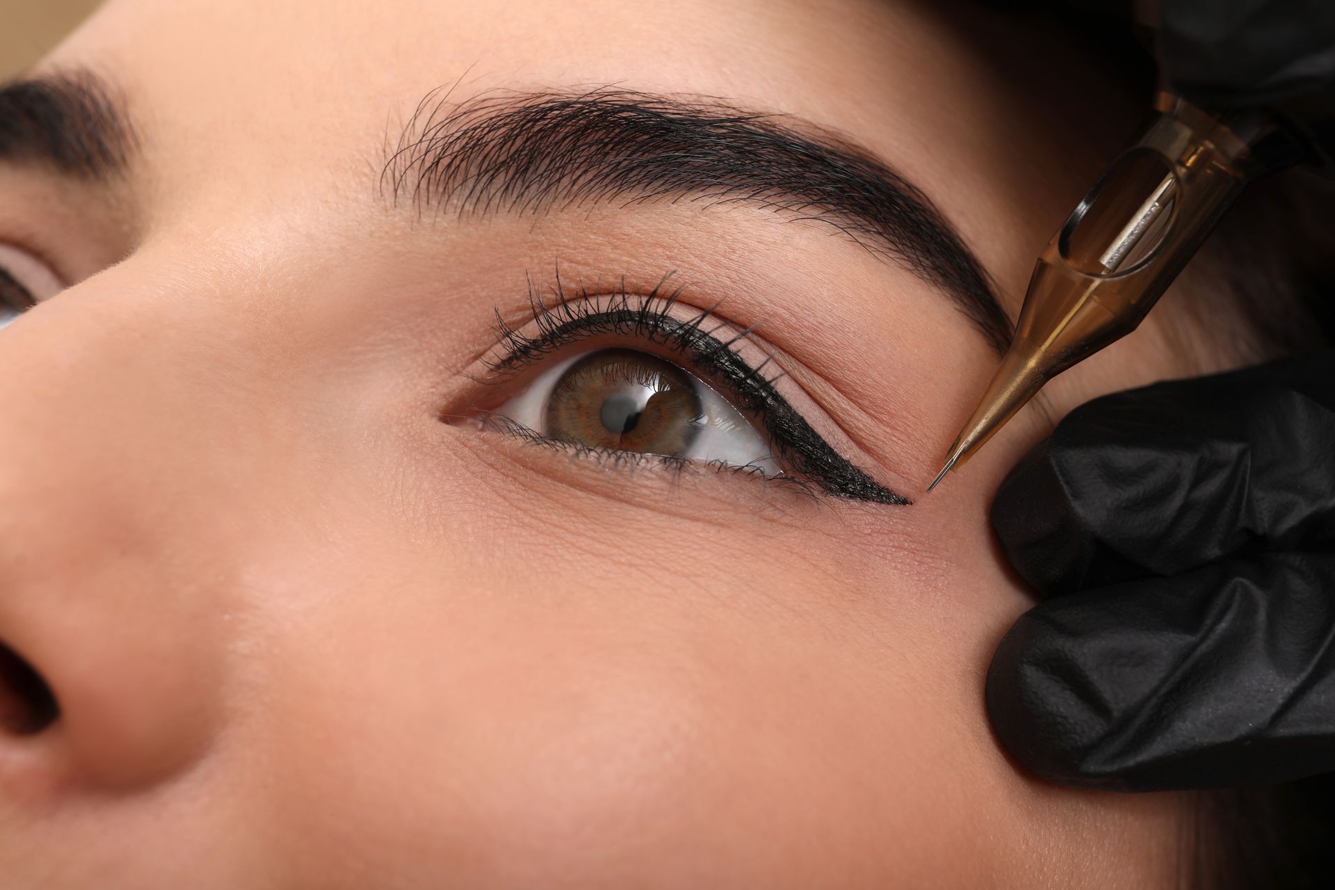 Eyeliner tattoo procedure, close-up of eye. Black eyeliner is being applied with a tattoo pen.