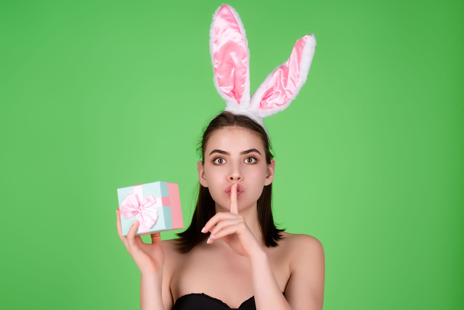 The woman is wearing bunny ears and holding a gift box while making the