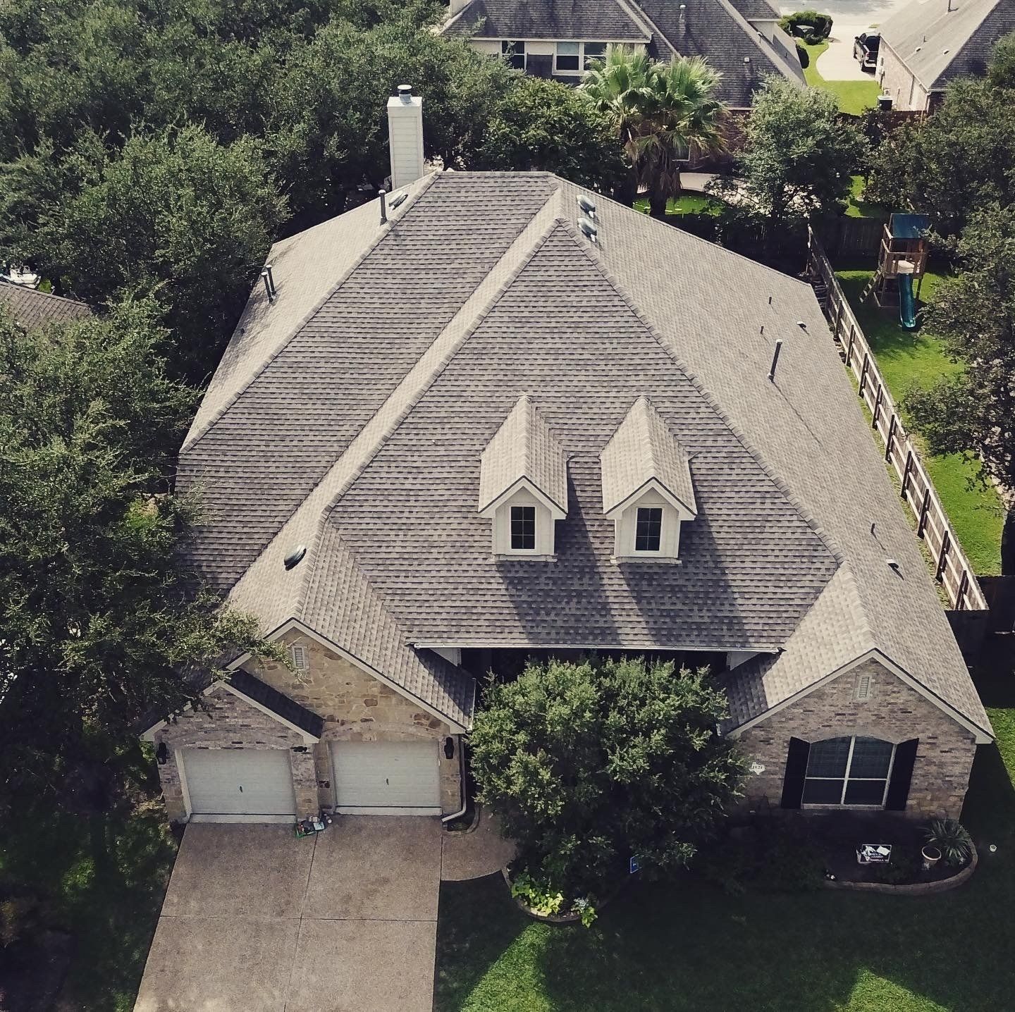 Aerial view of a gray shingled suburban house with a two-car garage and trees around it
